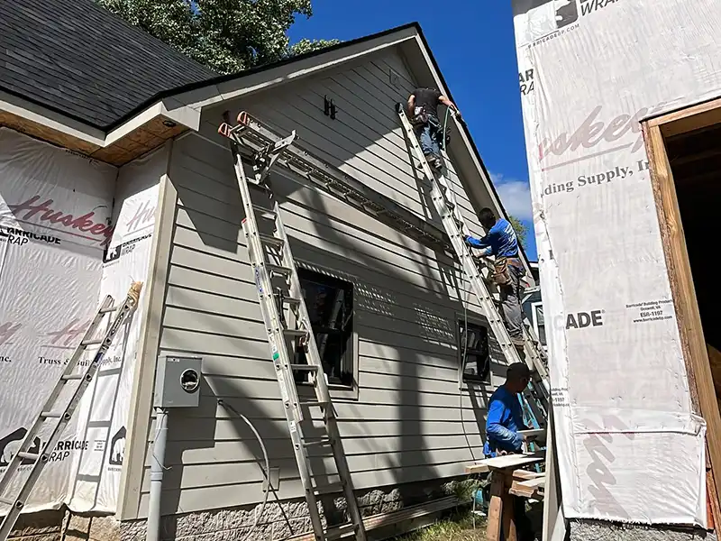 URCovered Construction workers installing light gray siding on a home